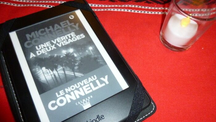 Liseuse avec la couverture du livre de Micahel Connelly, Une vérité à deux visages. Liseuse posée sur une nappe à côté d'un luminion.