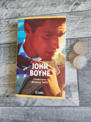 Le livre de John Boyne, l'audacieux monsieur swift, posé sur un parquet. A côté trois morceux de verre poli