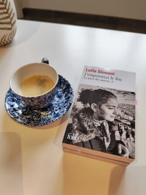 Une tasse à café à côté d'une pile de livres. Au-dessus de la pile de livre, celui de Leila Slimani, J'emporterai le feu.