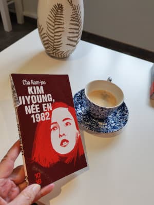 Une main tenant le livre de Cho Nam-Joo, Kim Jiyoung, née en 1982. Tasse de café et vase