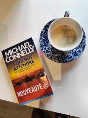 Le livre de posche de Michael Connelly, À qui sait attendre. Posé sur une table, à côté d'une tasse à café
