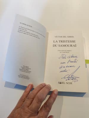 Une main tient le livre de Víctor del Árbol, La tristesse du samourai. Le livre est ouvert sur la page de dédicace